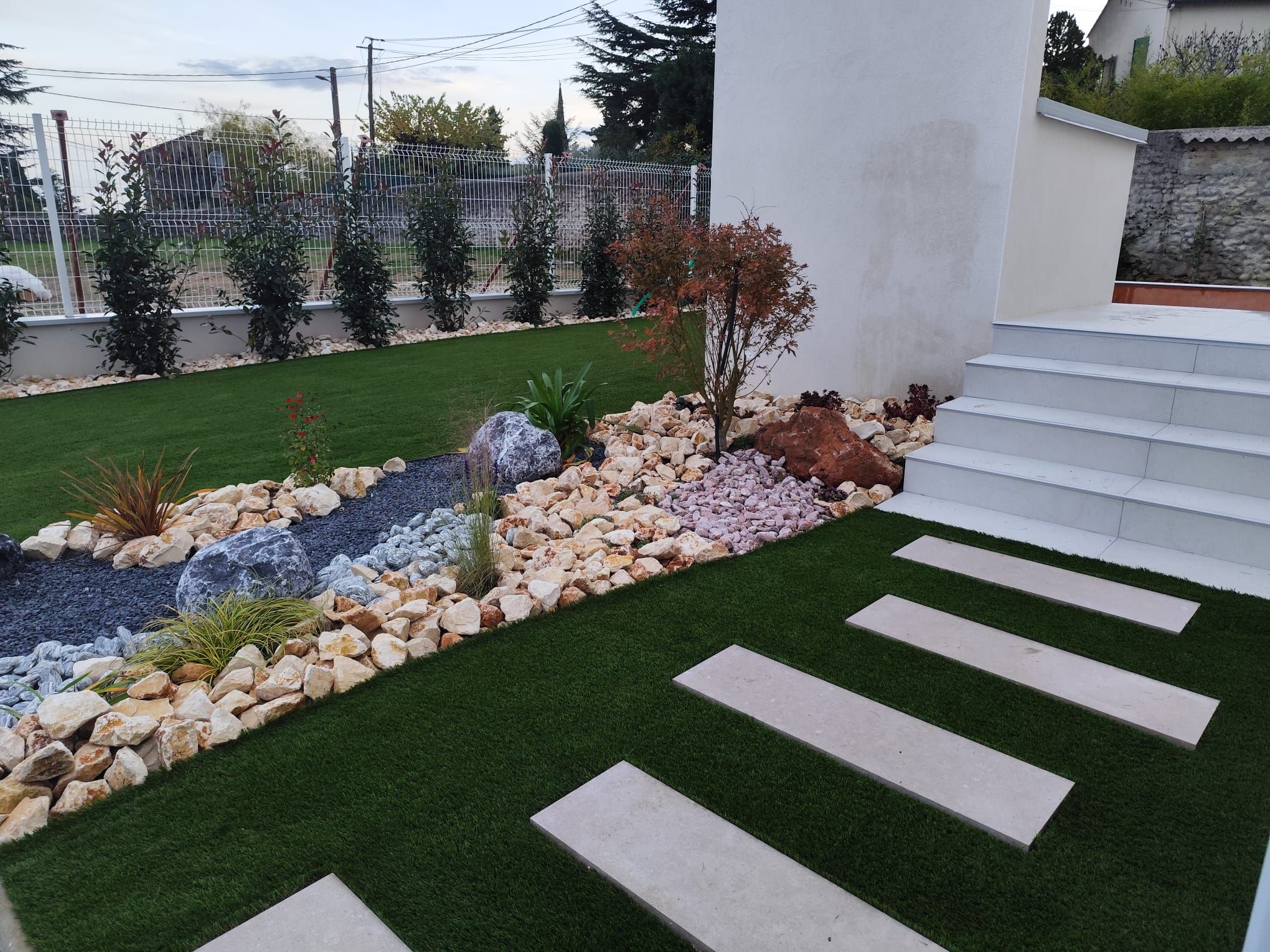 Jardin en gazon synthétique avec pas japonais et massif minéral au pied d’un escalier