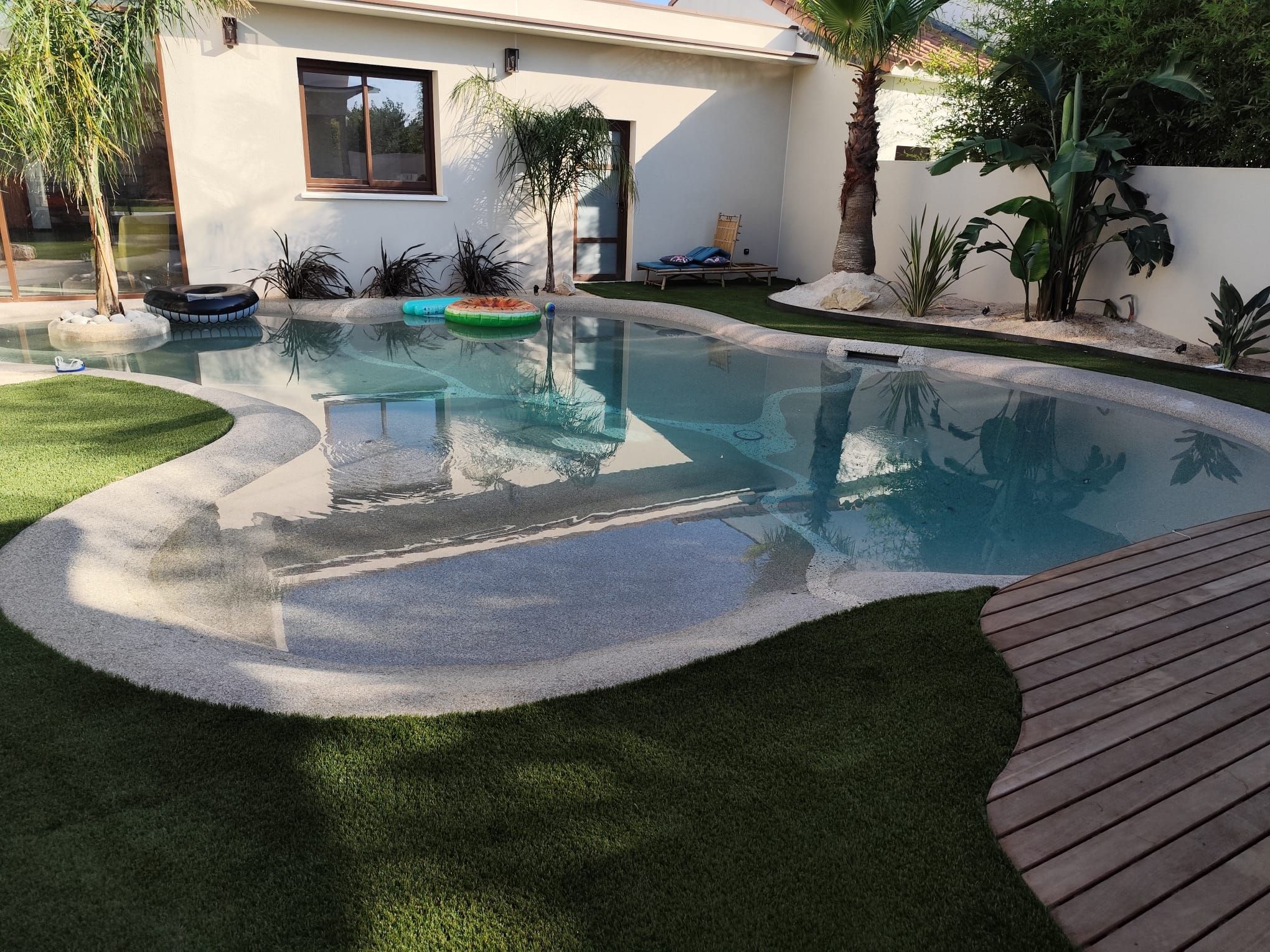 Piscine à plage immergée bordée de gazon synthétique et d’un deck en bois