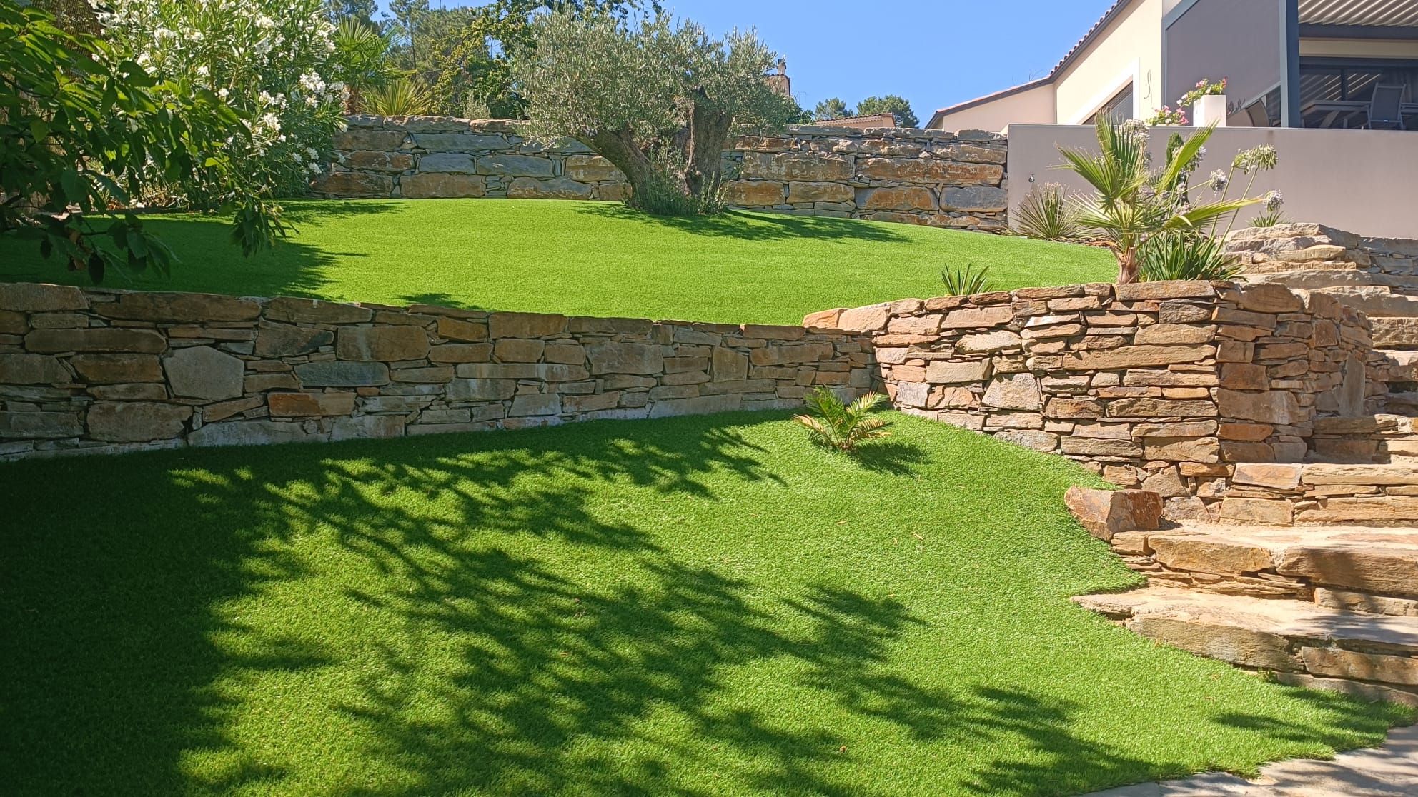 Jardin en terrasses avec murets en pierre sèche et gazon synthétique