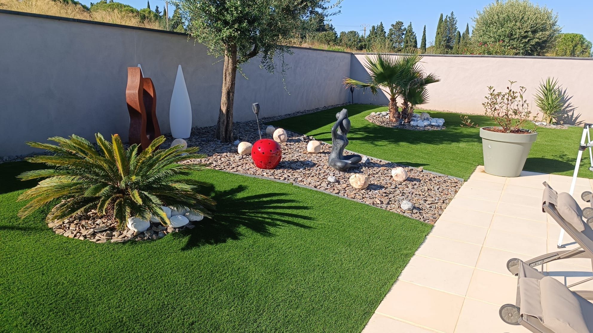 Jardin contemporain en gazon synthétique avec massif de galets et sculptures
