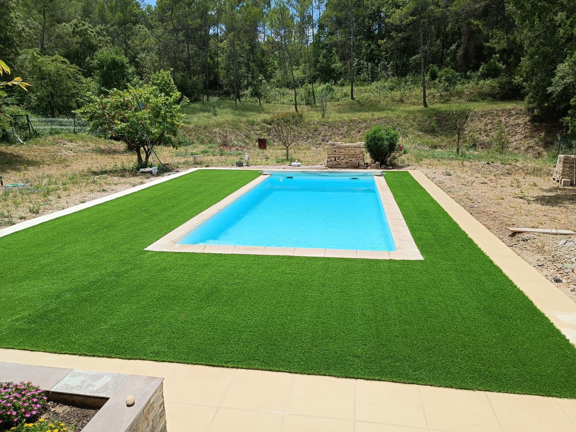 Piscine rectangulaire encadrée de gazon synthétique en lisière de bois