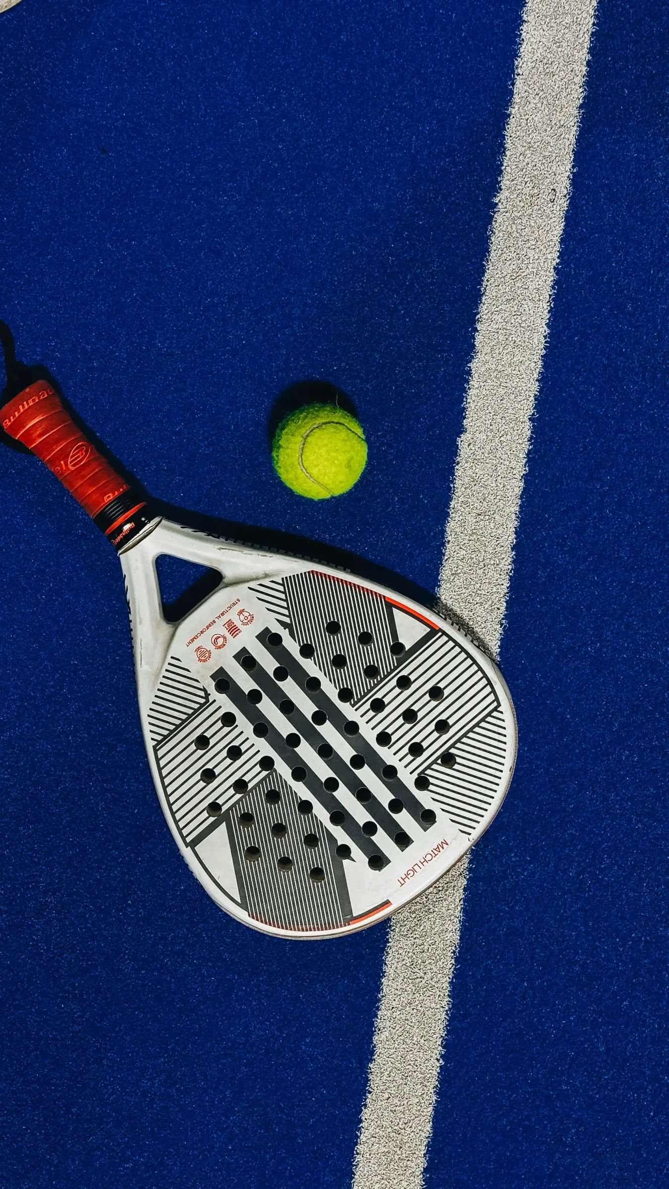 Raquette et balle de padel sur un terrain en gazon synthétique bleu